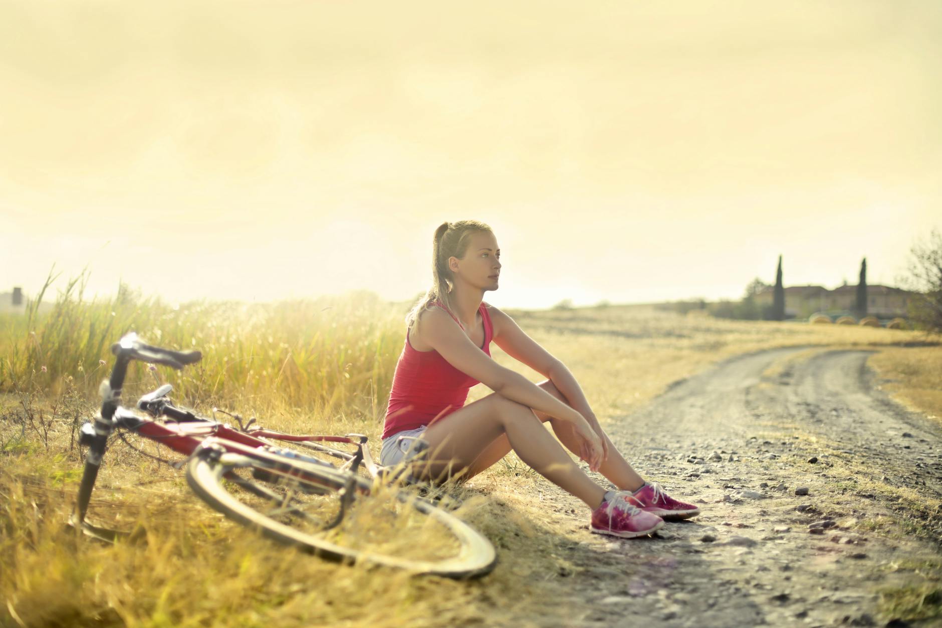 photo of woman in red tank top sitting by the side of a dirt road next to a her bike