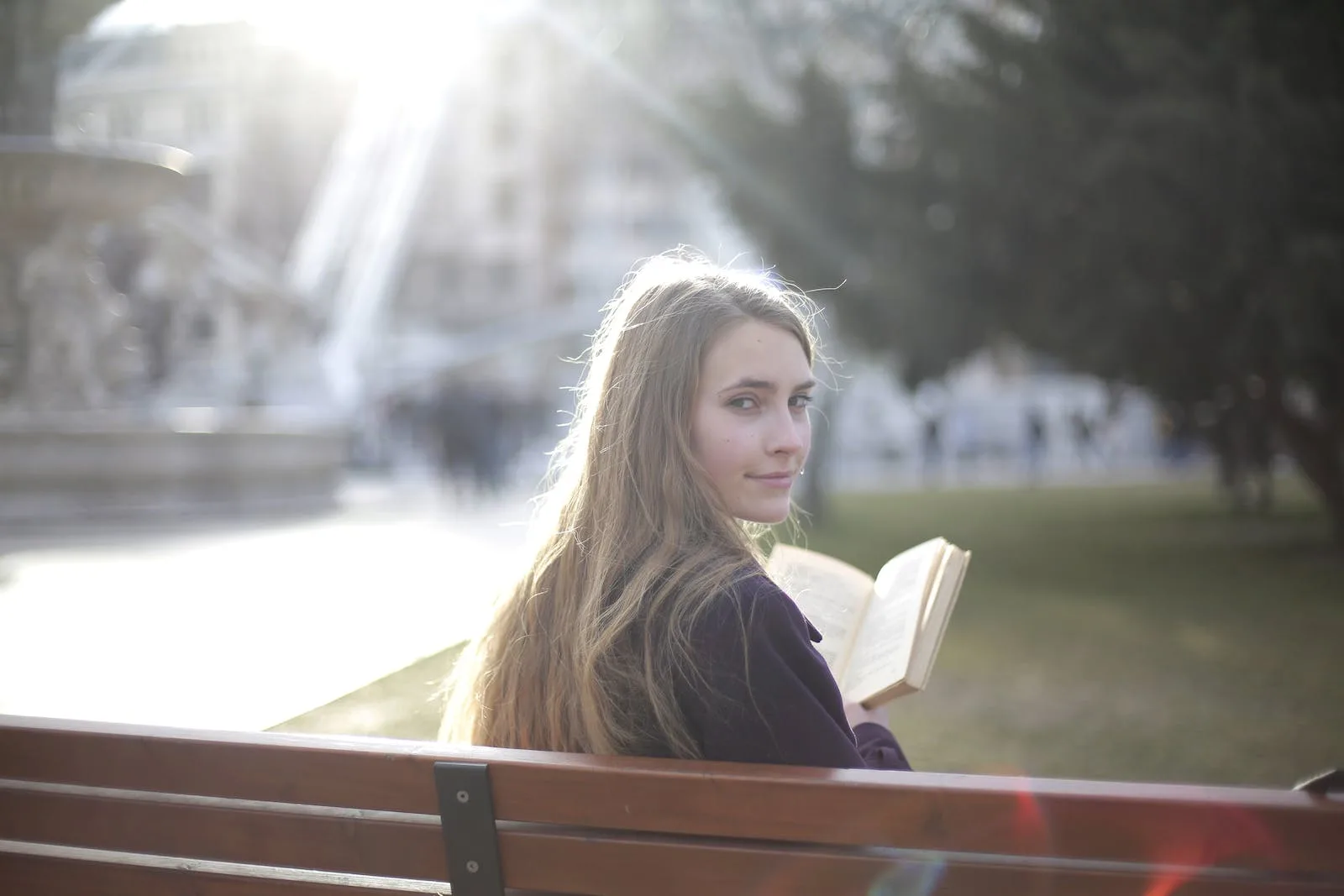 back view of peaceful female in casual jacket sitting on wooden bench in city park and enjoying story while relaxing and looking over shoulder