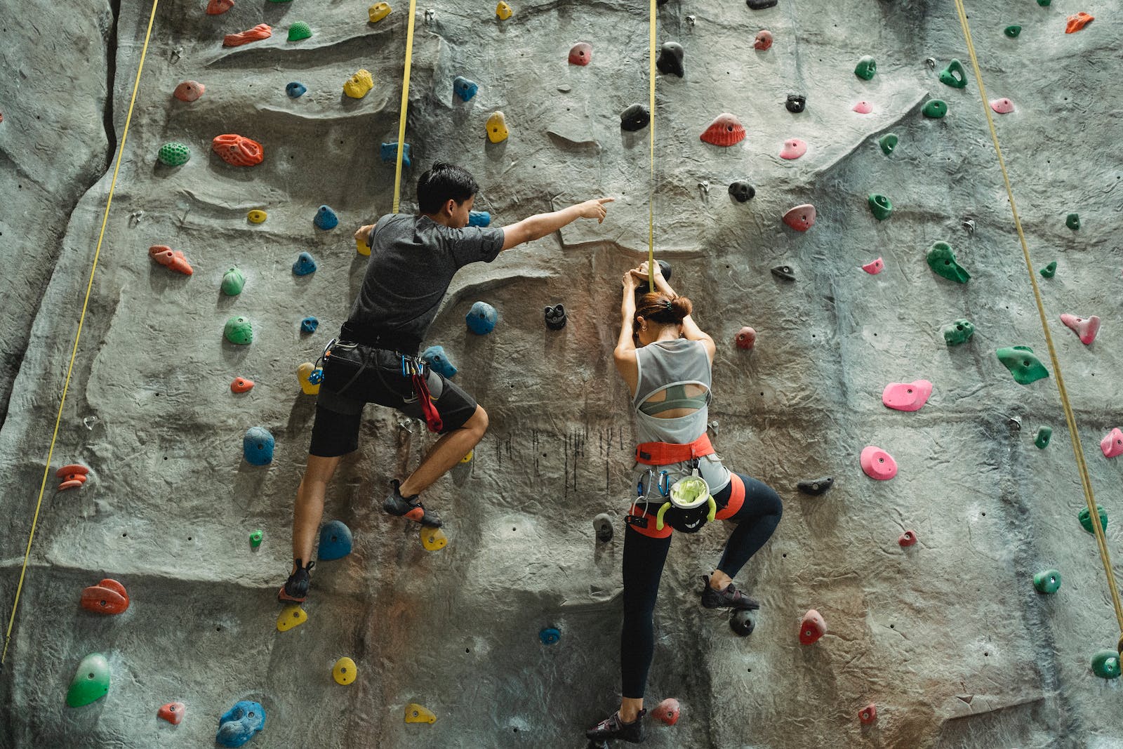 Back view of faceless mountaineers in sportswear with belay training climbing on wall