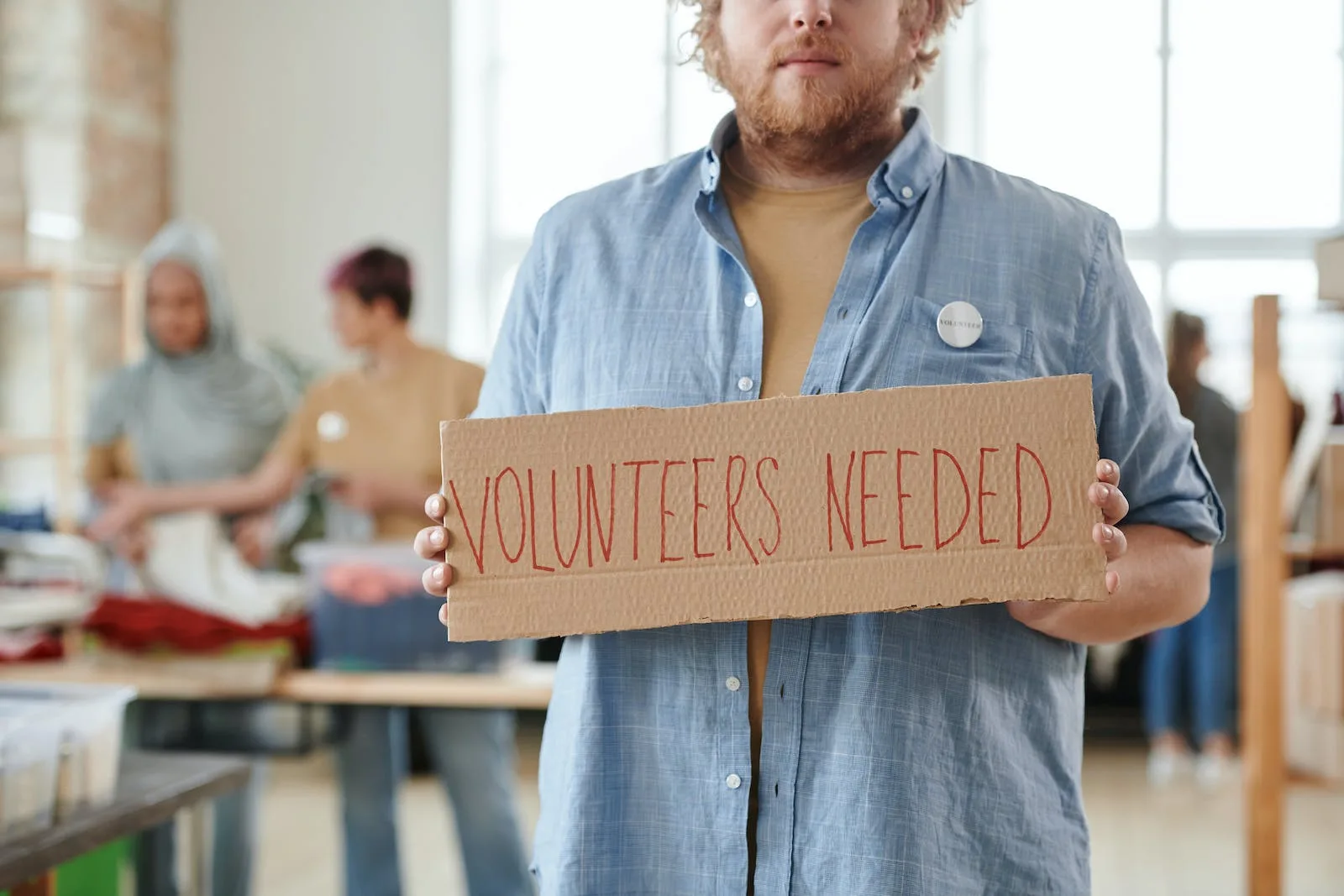 man holding a sign saying volunteers needed
