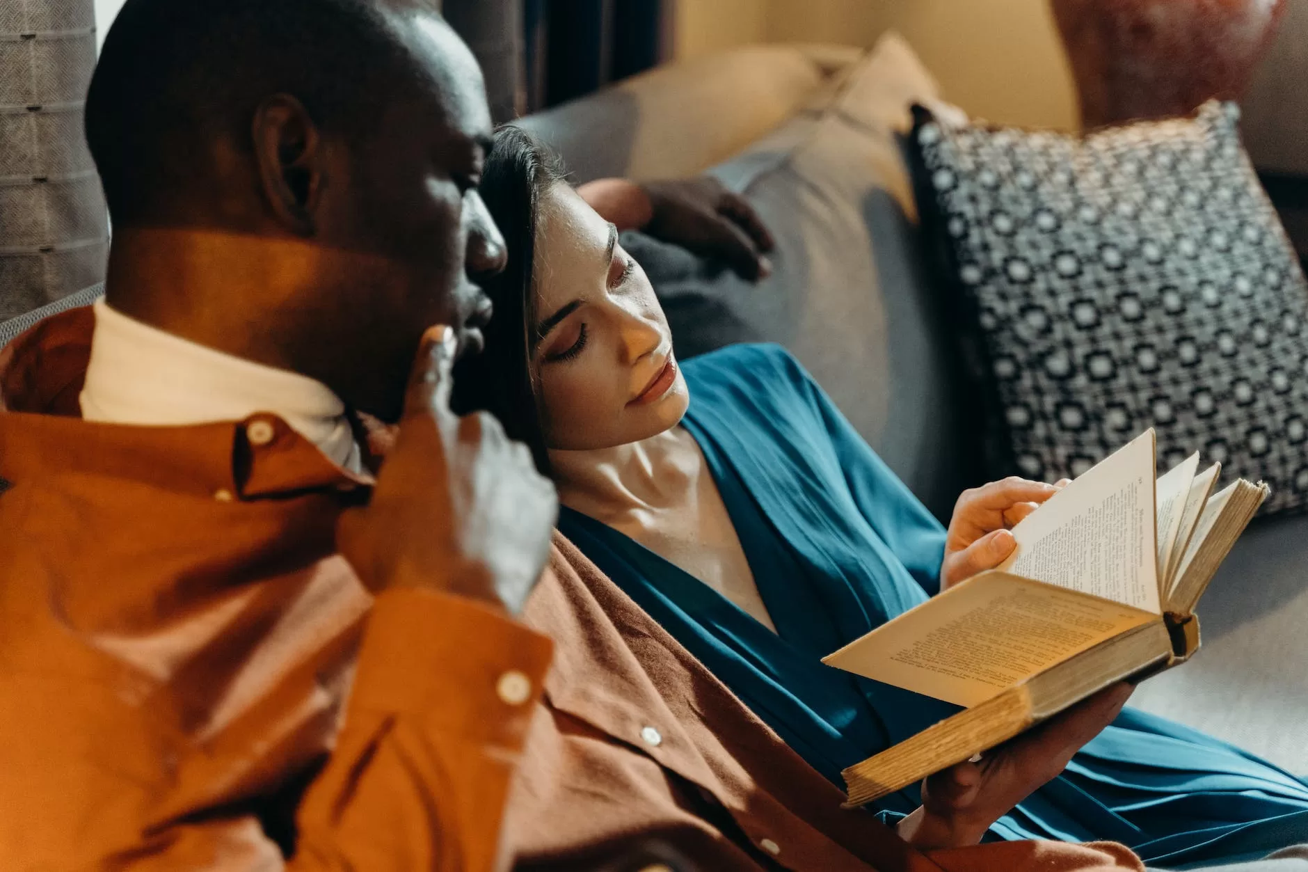 couple sitting on gray couch reading book