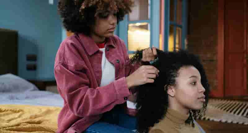 Young Woman in Pink Jacket brading her Sister's Hair