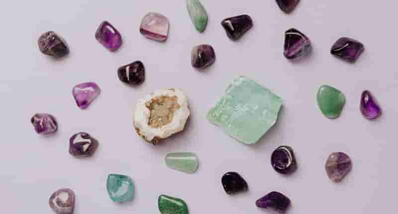 Flat lay of assorted polished gemstones including amethyst and jade on a light background.