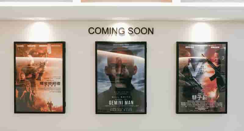 Framed posters of upcoming movies in a cinema hallway under 'Coming Soon' sign.