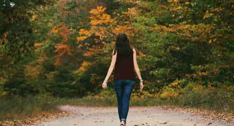 A young woman walks down a colorful autumn forest path, surrounded by vibrant leaves.