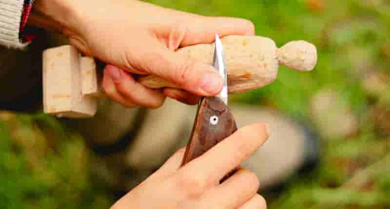 Person skillfully carving a wooden figure with a knife in a serene outdoor setting.