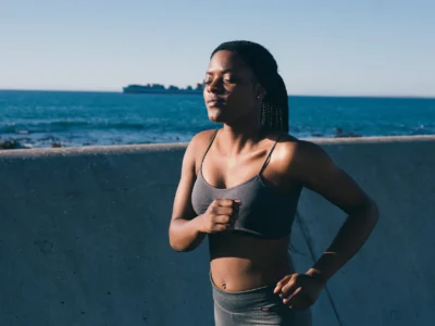 photo of woman in gray spaghetti strap top and gray pants running beside concrete wall