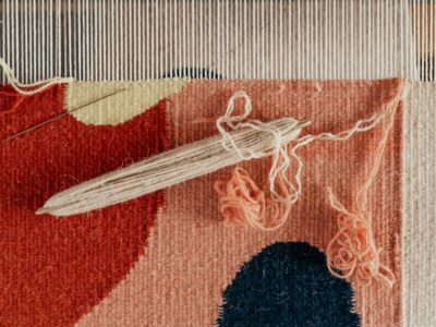 From above of shuttle and needle placed on part of handmade carpet with circle pattern on loom frame during weaving process