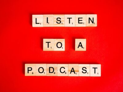 Scrabble tiles on red background forming the phrase 'Listen to a Podcast'.