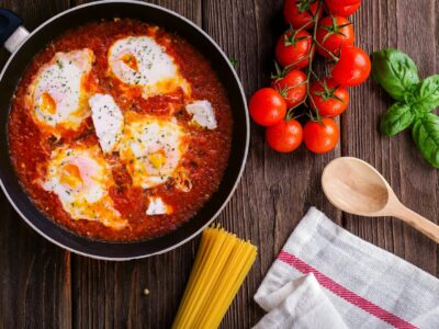 Delicious eggs in tomato sauce with basil, spaghetti, and fresh tomatoes on a wooden table.