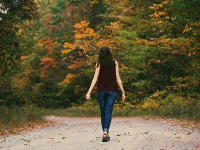 A young woman walks down a colorful autumn forest path, surrounded by vibrant leaves.