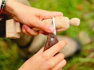 Person skillfully carving a wooden figure with a knife in a serene outdoor setting.